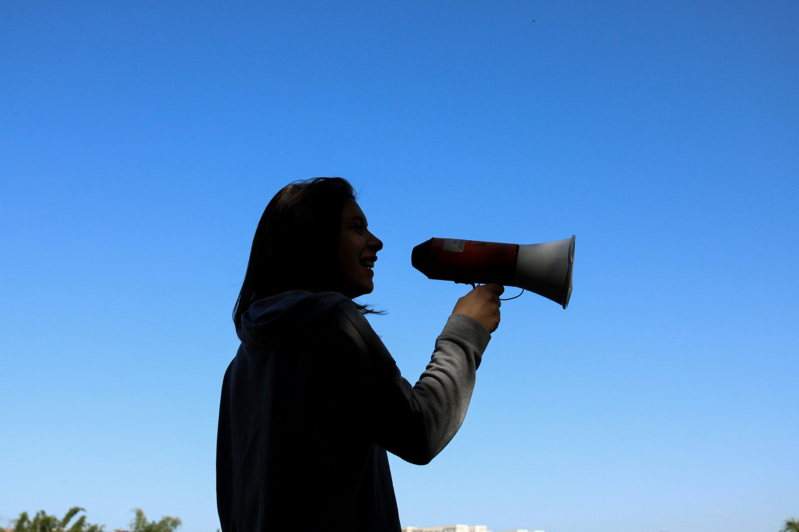 Frau spricht durch ein Megafon vor blauem Himmel